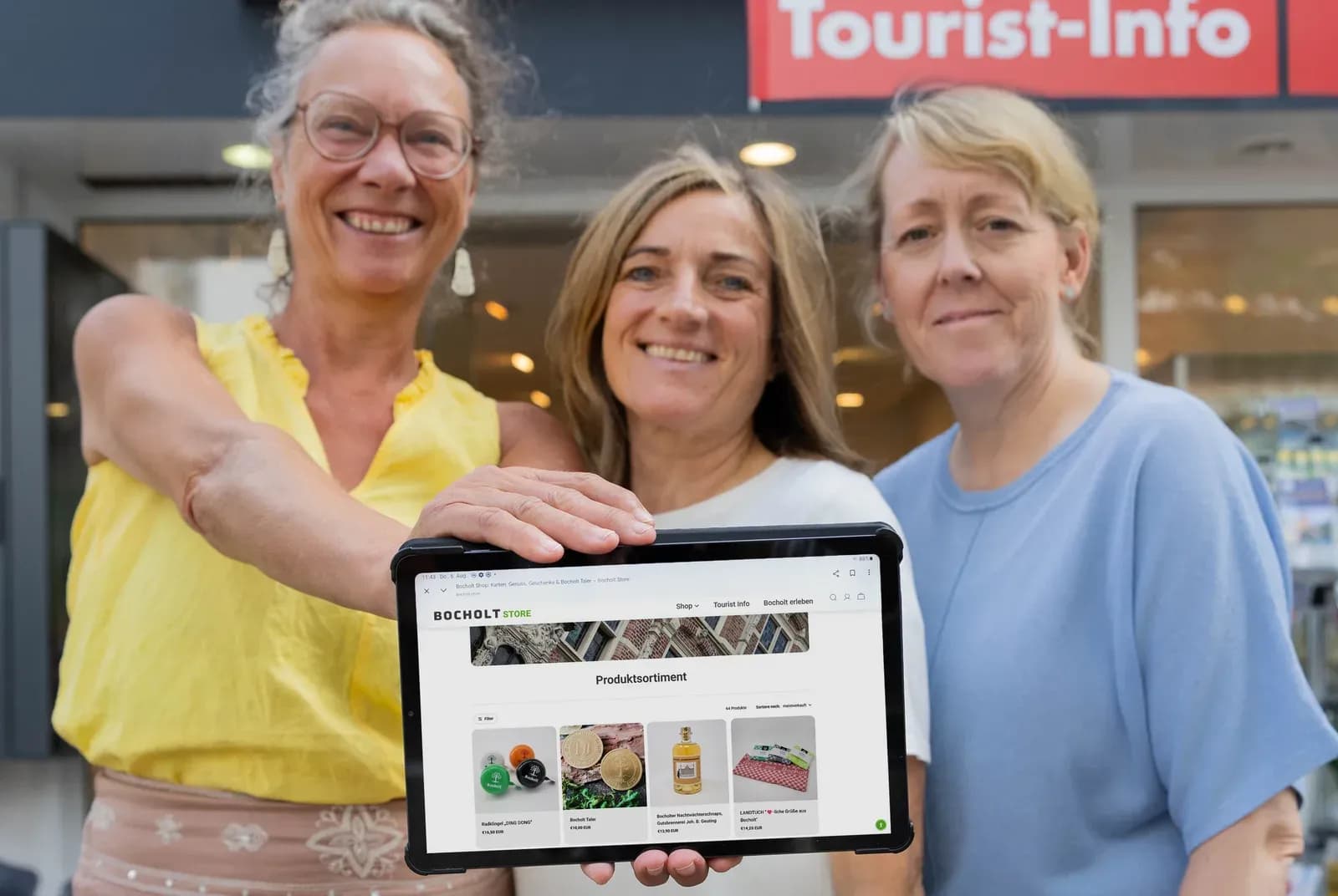 Drei Mitarbeiterinnen der Tourist-Info Bocholt halten ein Tablet mit dem Produktsortiment von bocholt.store in die Kamera