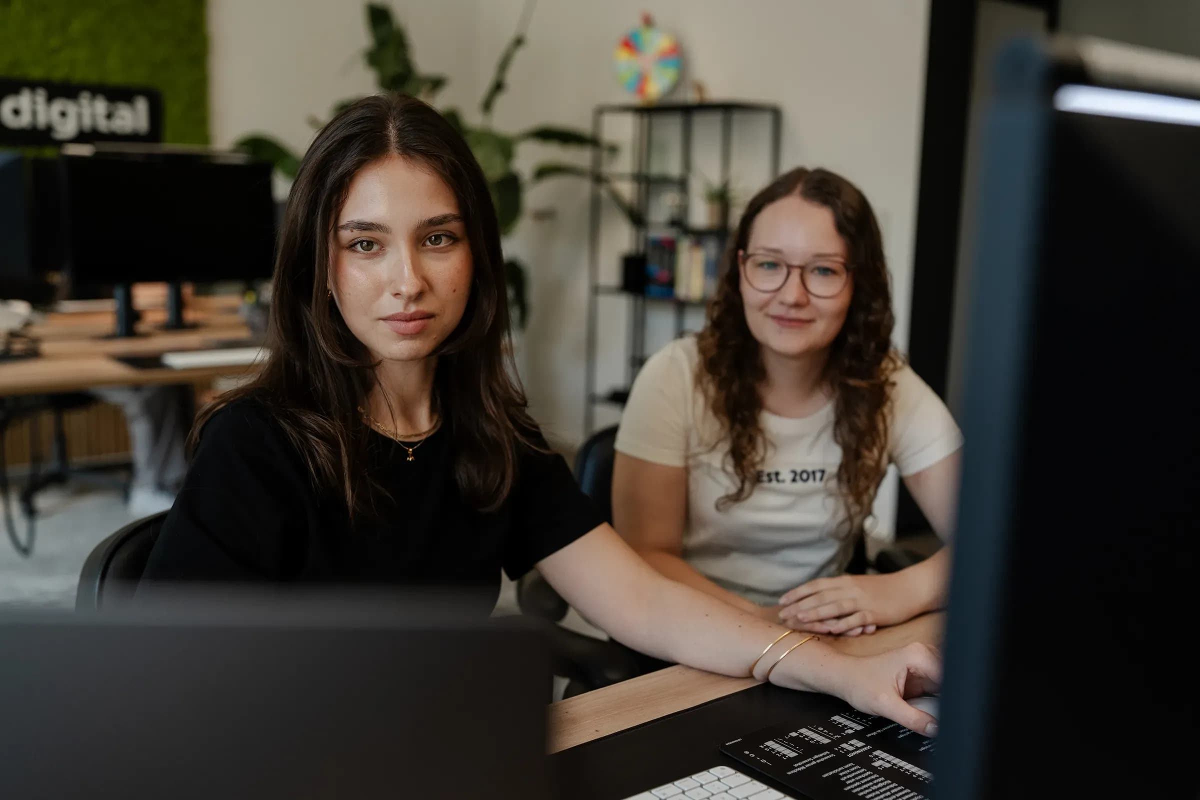 Zwei Kolleginnen von skeon digital am Arbeitsplatz blicken in die Kamera