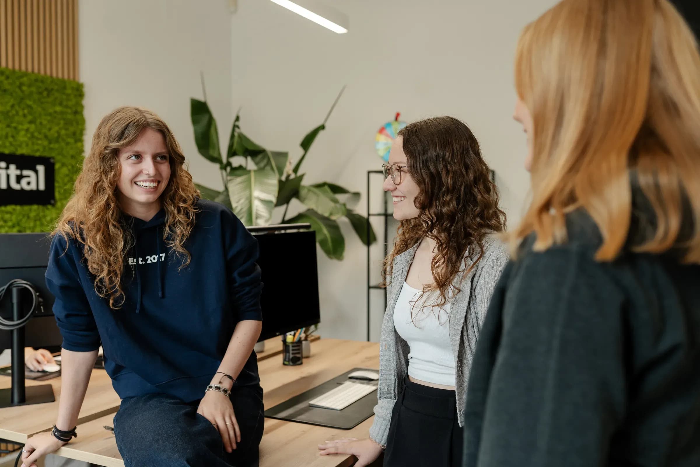 Zwei Kolleginnen von skeon digital im Gespräch, eine sitzt auf dem Schreibtisch