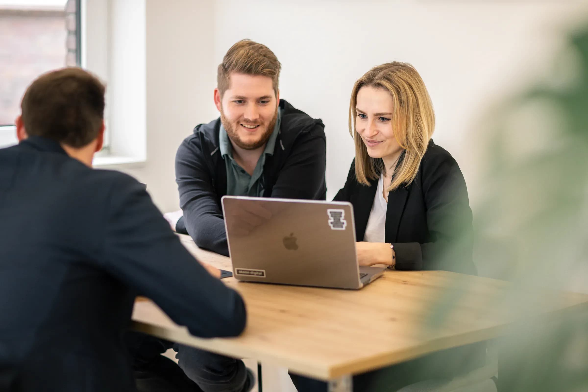 Drei Teammitglieder von skeon digital am Laptop im Gespräch am Besprechungstisch