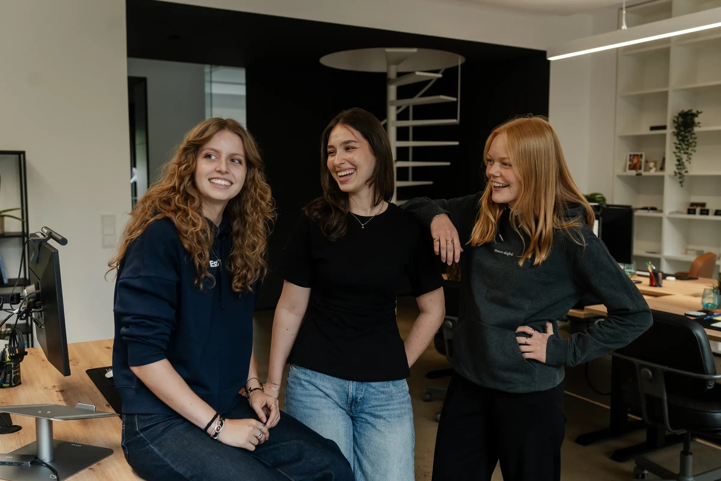 Drei Kolleginnen von skeon digital stehen lachend zusammen im Büro