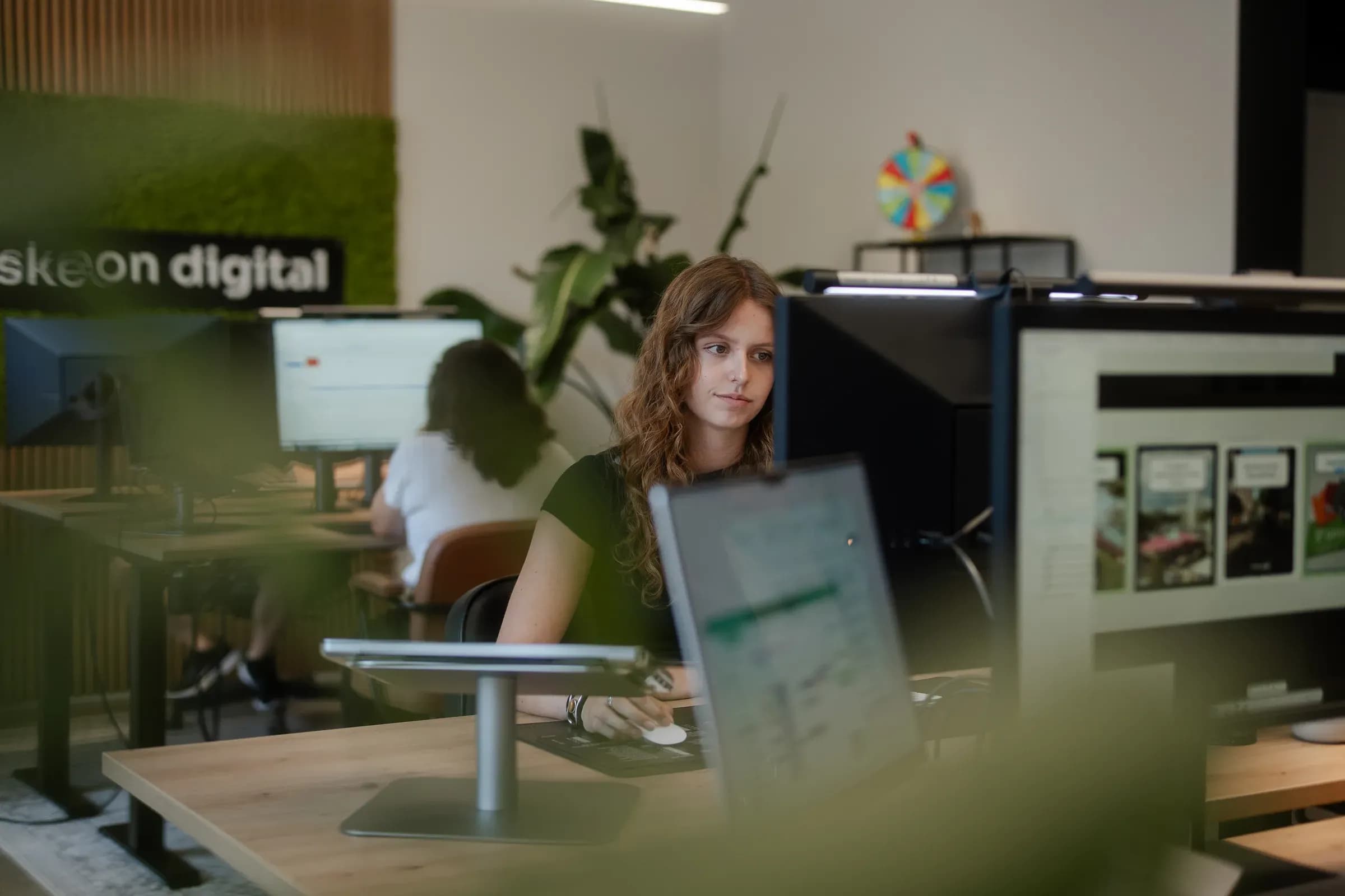 Kollegin am Monitor mit Social-Media-Beiträgen, im Hintergrund die Mooswand von skeon digital