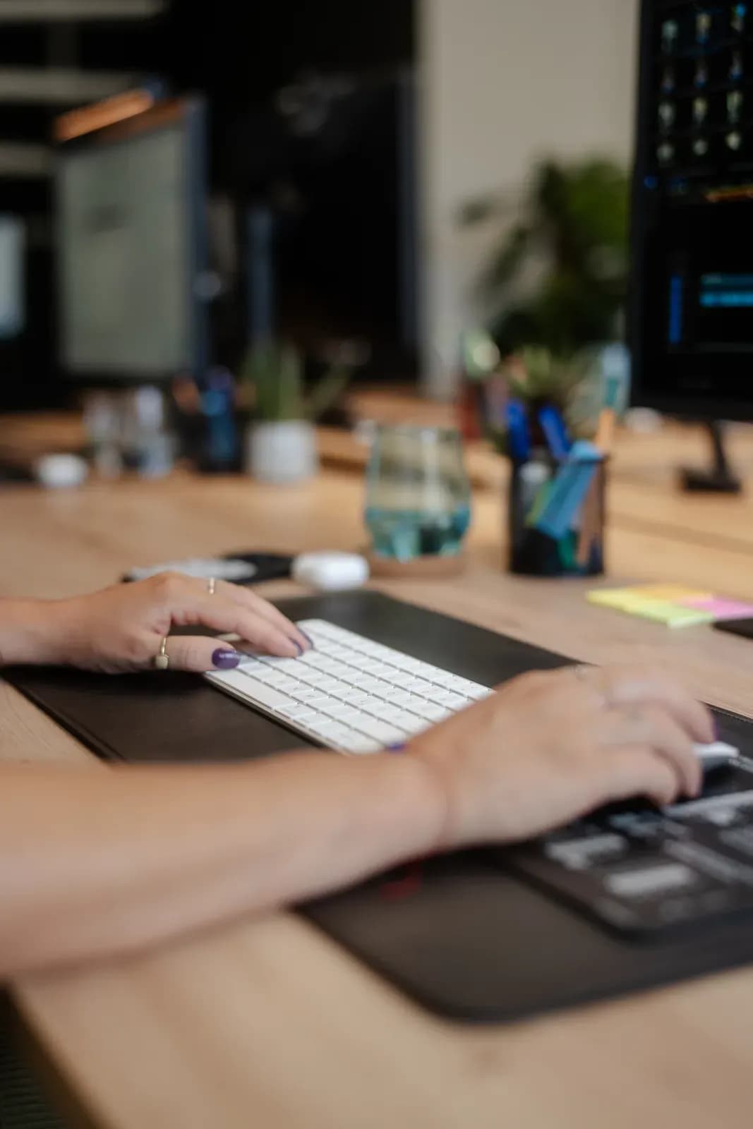Hände an einer Tastatur am Schreibtisch bei skeon digital, im Hintergrund Monitore mit Auswertungen