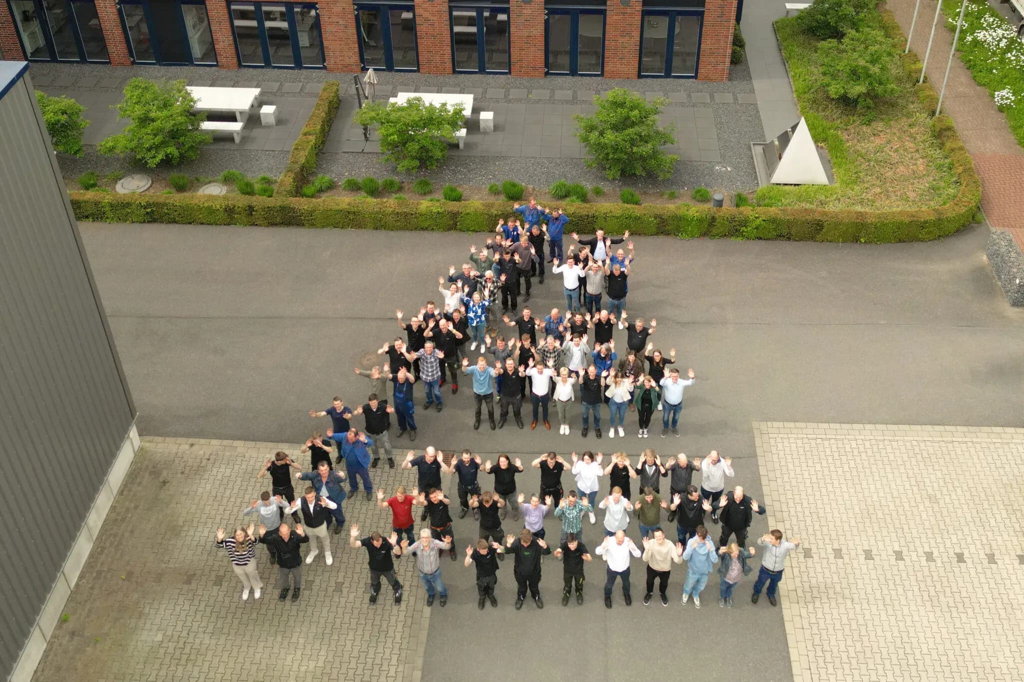 Luftaufnahme: Das Team von Spaleck Oberflächentechnik winkt auf dem Firmenhof vor dem Verwaltungsgebäude