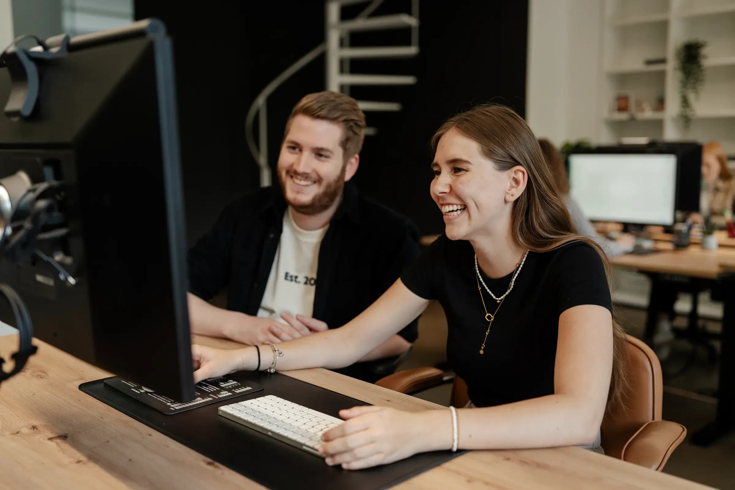 Zwei Teammitglieder von skeon digital lachen gemeinsam vor dem Monitor