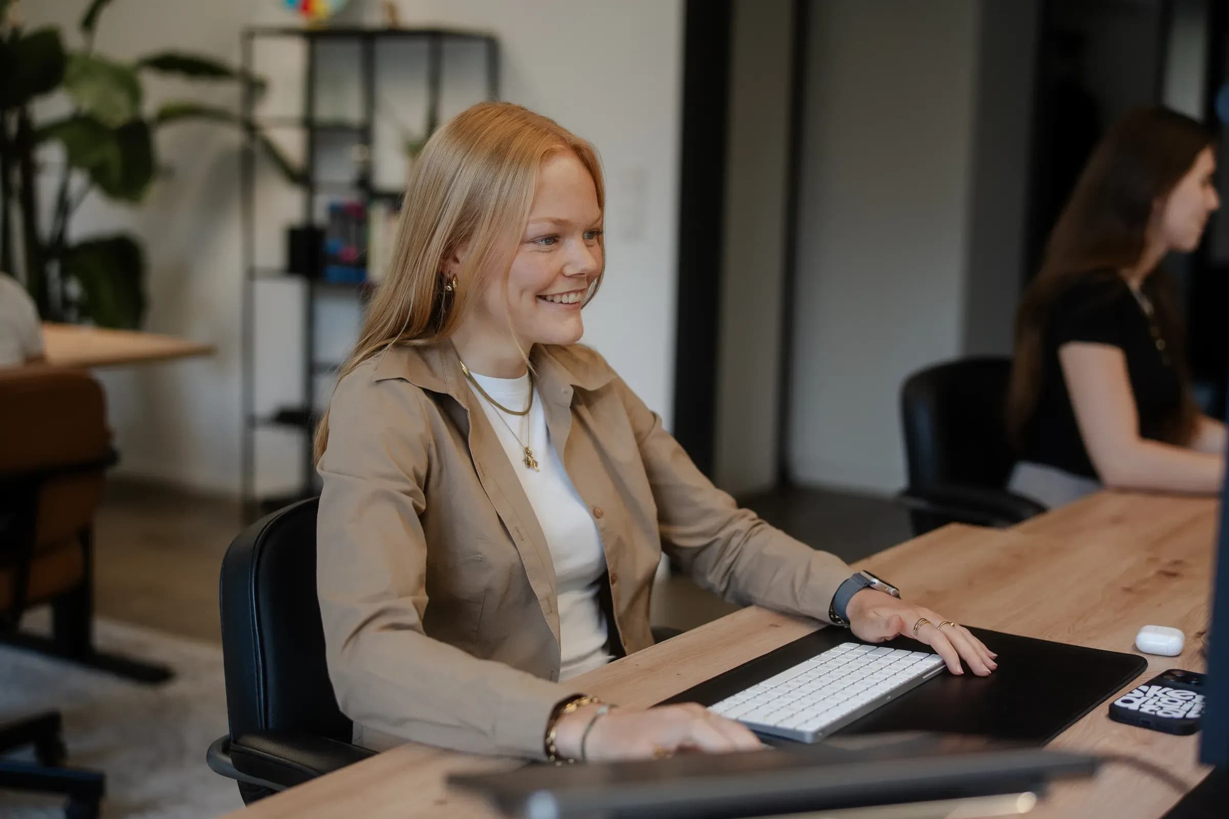 Kollegin von skeon digital lächelnd am Schreibtisch, im Hintergrund eine Kollegin