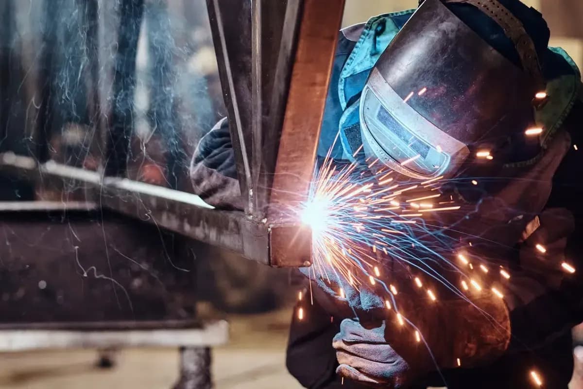 Schweißer mit Schutzhelm bei der Arbeit an einer Stahlkonstruktion, Funken fliegen