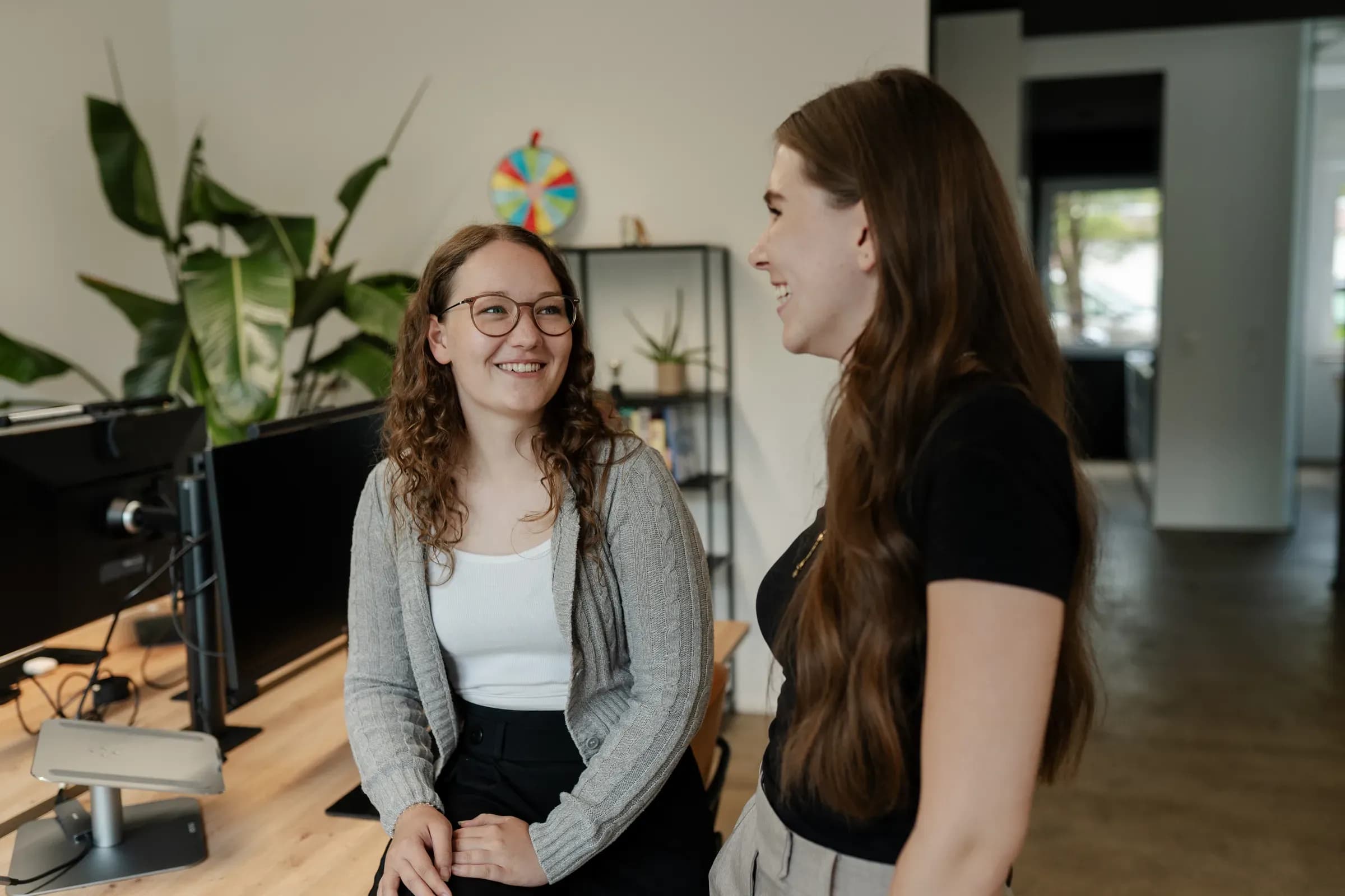 Zwei Kolleginnen von skeon digital im Gespräch zwischen den Schreibtischen