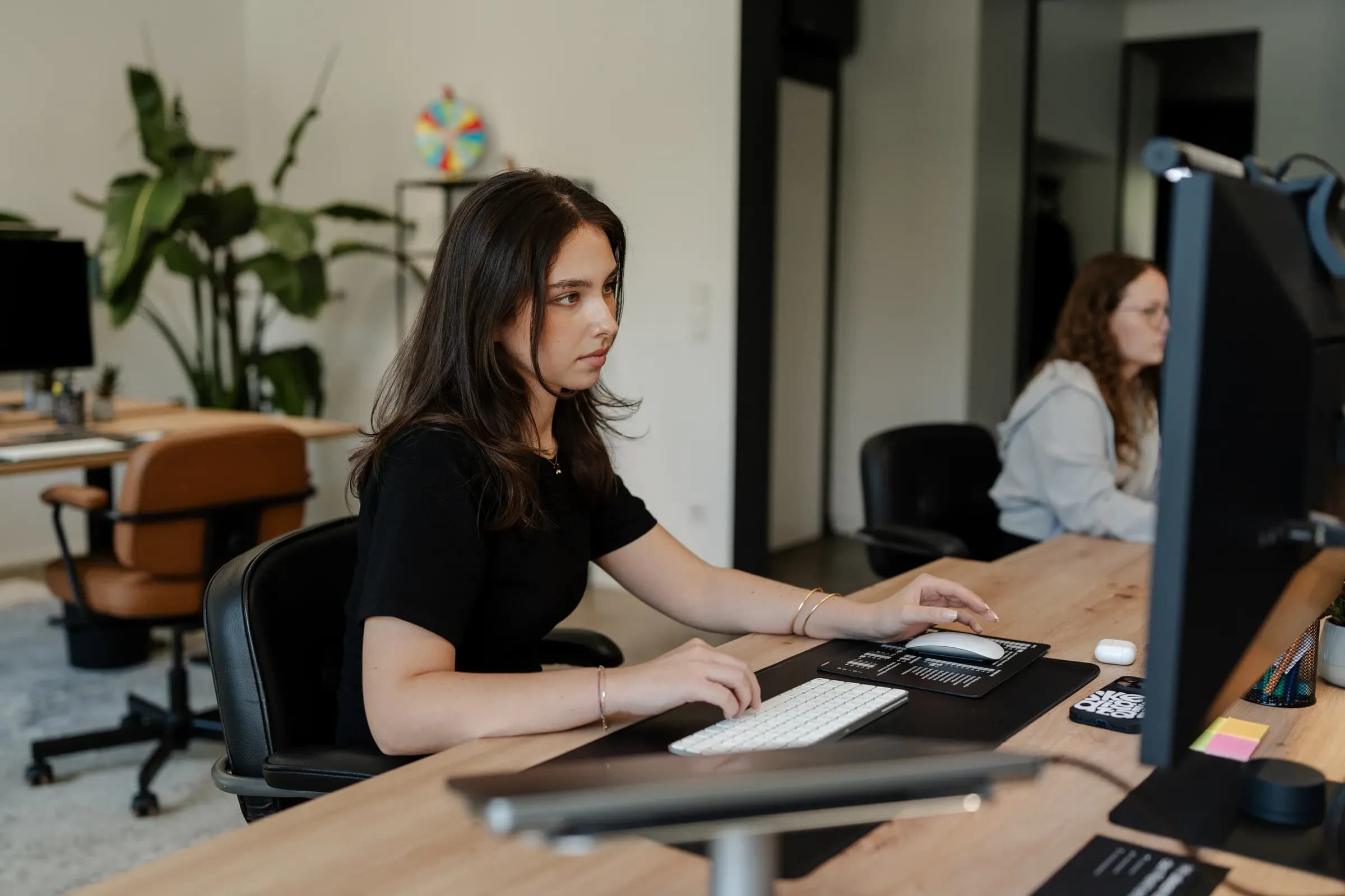 Kollegin von skeon digital arbeitet konzentriert am Monitor, im Hintergrund eine Kollegin am Nachbarplatz
