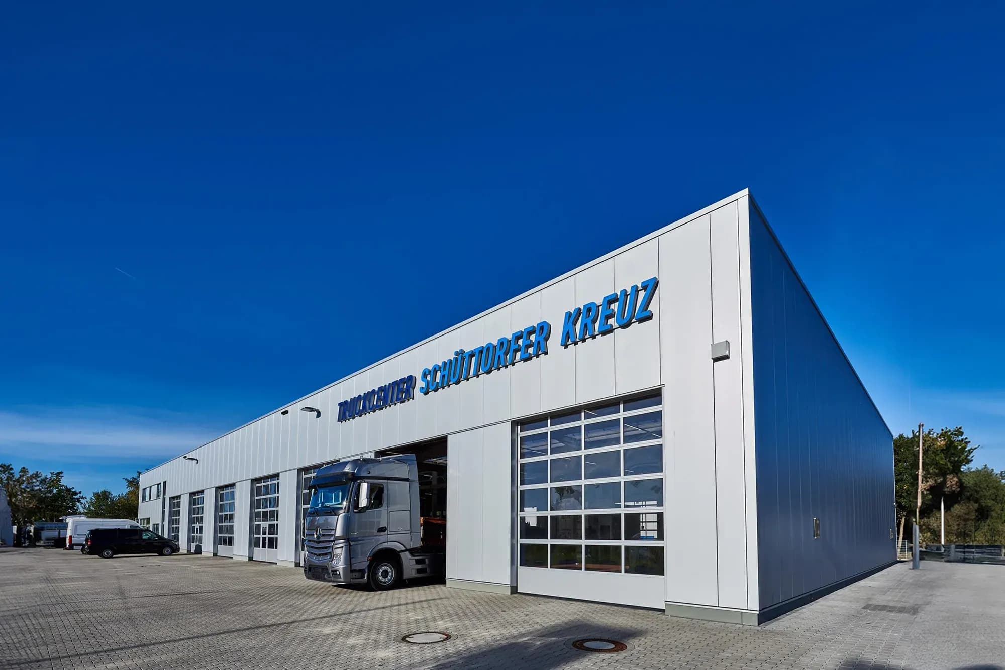 Werkstatthalle des Truckcenters Schüttorfer Kreuz mit Schriftzug an der Fassade, ein Lkw steht in einer der Durchfahrten, blauer Himmel