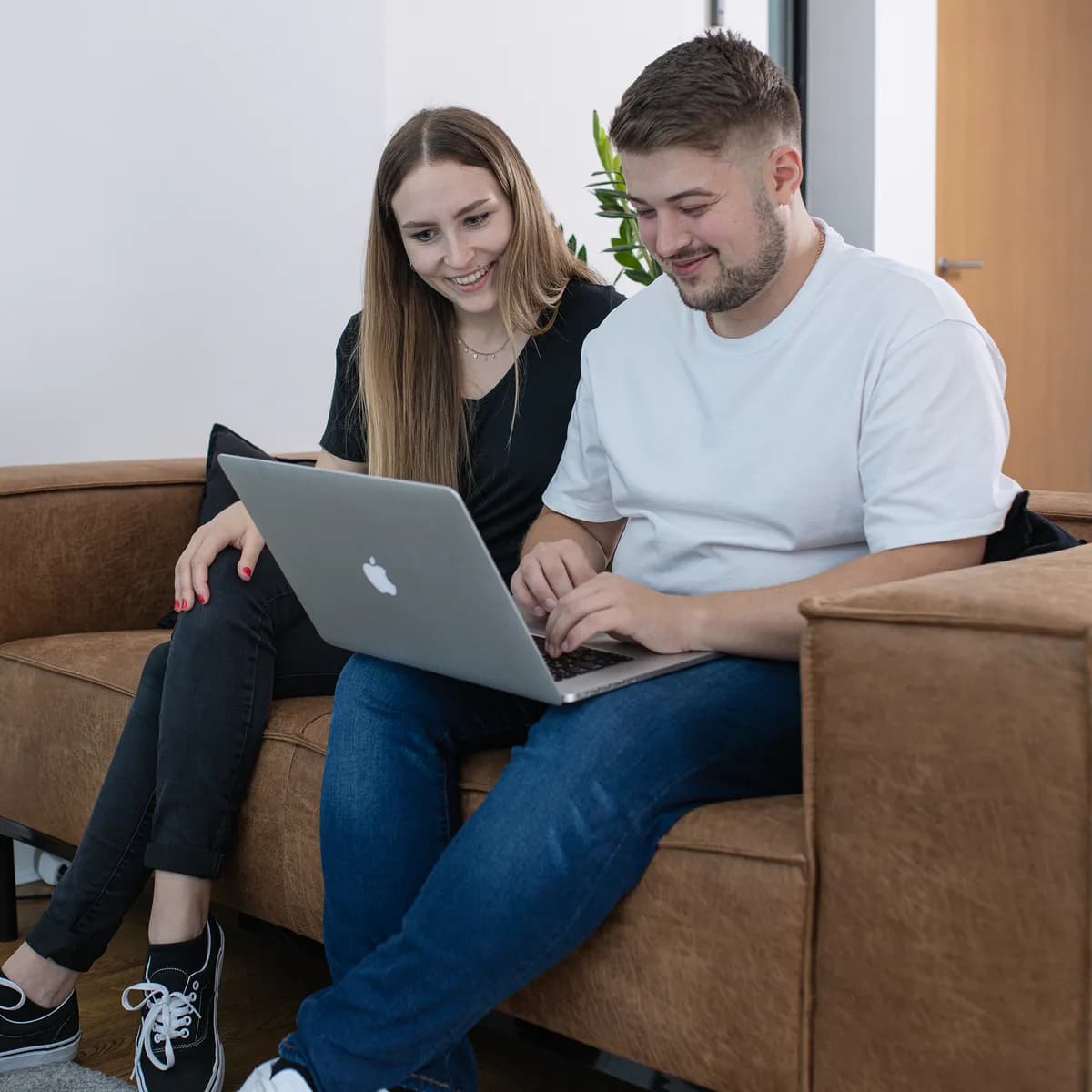 Zwei Teammitglieder sitzen mit einem Laptop auf dem Sofa und lachen